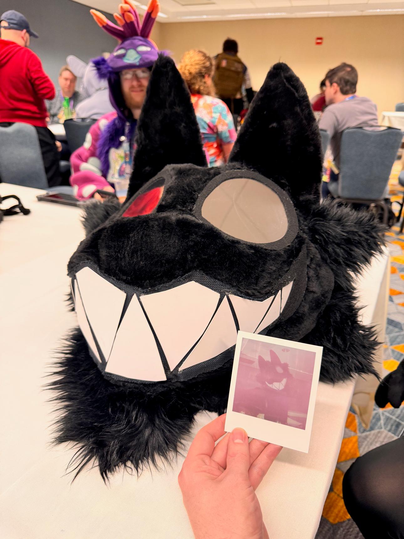 A dark toothy fursuit head is next to a faded polaroid