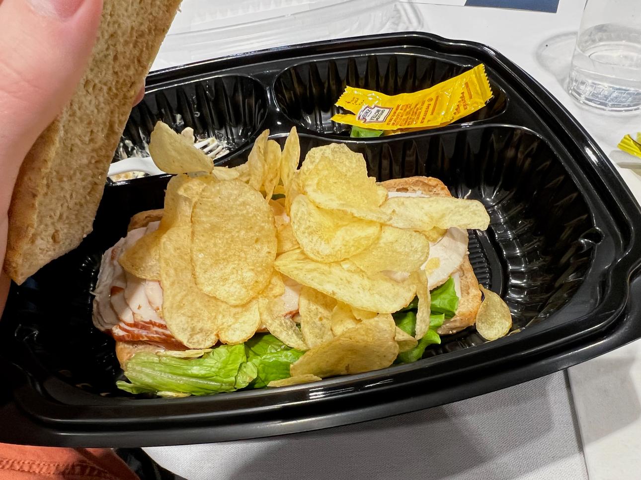 A picture of a ham sandwich with some chips tossed on top of the ham.
